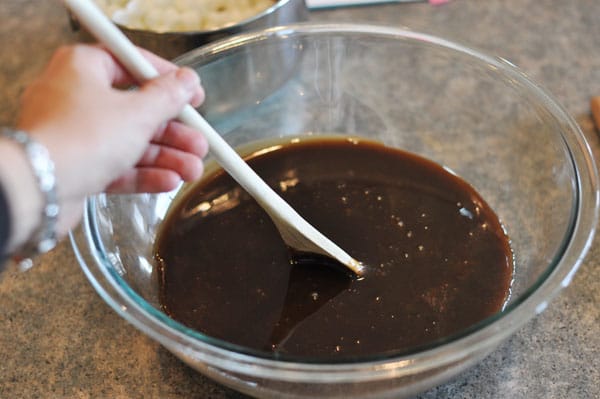 dark fudge mixture in a glass bowl being stirred by a wooden spoon