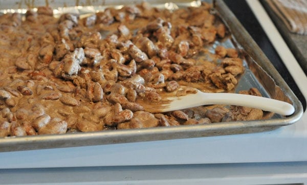 candy coated almonds being stirred on a cookie sheet with a wooden spoon