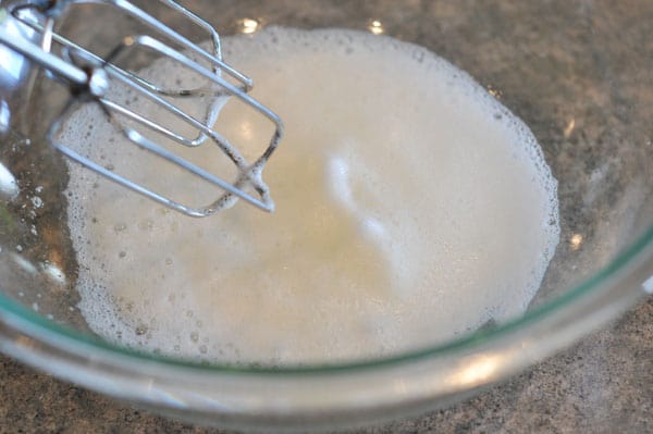 egg whites getting beaten and foamy in a glass bowl