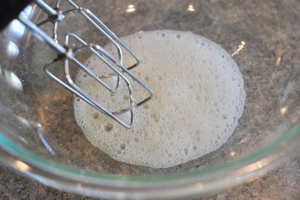 frothy egg whites in a glass bowl with beaters whipping them