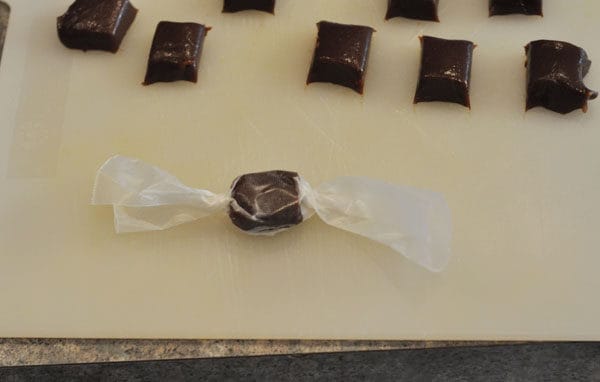 small square of chocolate caramel on a white cutting board with one wrapped in parchment paper