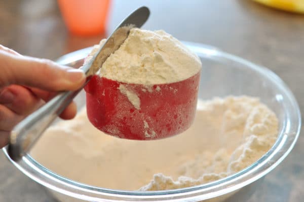 a butter knife leveling off flour in a red measuring cup