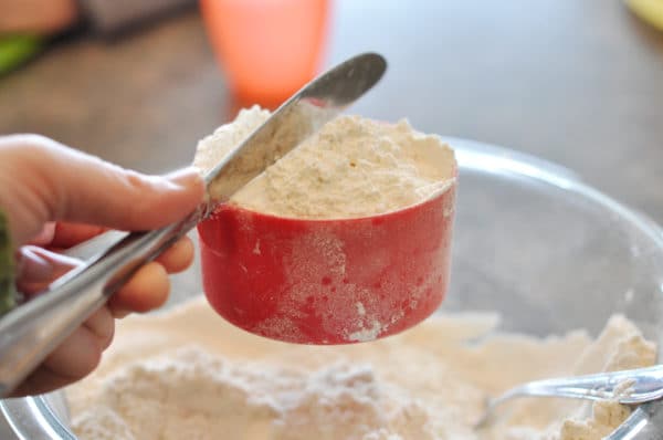 a red measuring cup full of white flour being leveled off with a butter knife