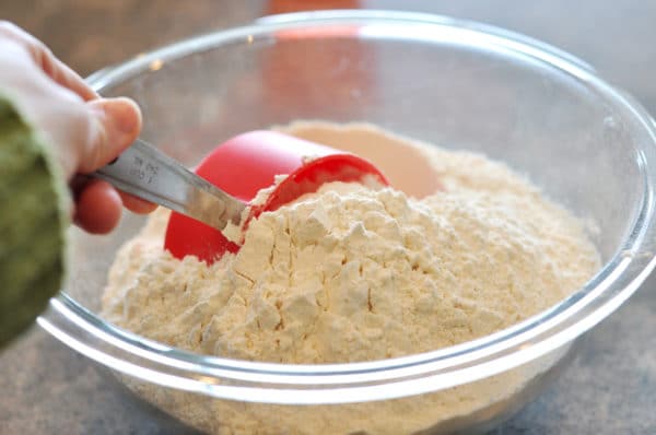 a red measuring cup scooping flour out of a glass bowl