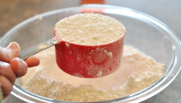 a red measuring cup full of white flour over a glass bowl of flour