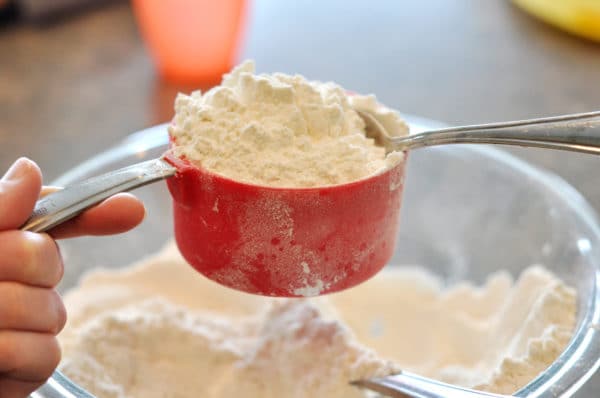 a spoon scooping white flour into a red measuring cup