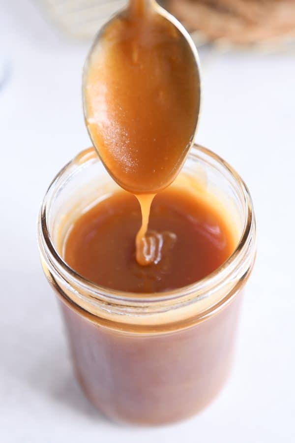Spoon drizzling homemade caramel sauce into glass jar.
