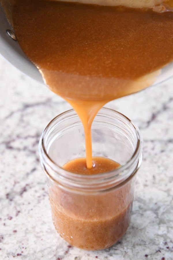 Pouring homemade caramel sauce into glass jar.