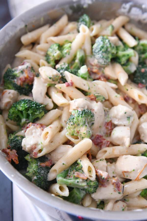 pasta, broccoli, sun-dried tomatoes and creamy sauce in stainless steel pot