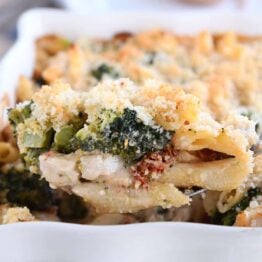 serving spoon taking scoop of baked penne out of white dish