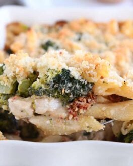 serving spoon taking scoop of baked penne out of white dish