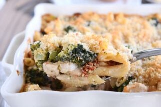 serving spoon taking scoop of baked penne out of white dish