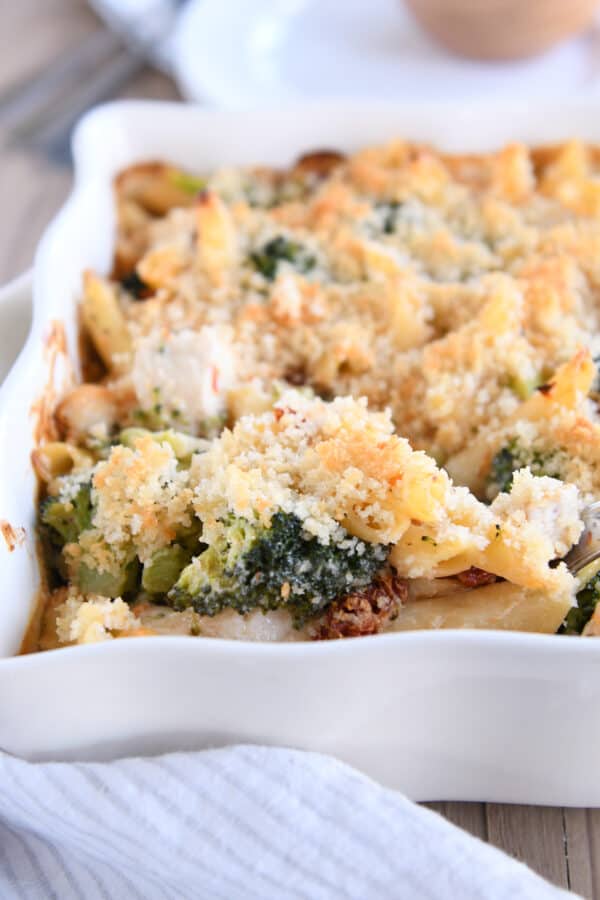 Serving spoon with scoop of baked penne and bread crumbs in white dish.