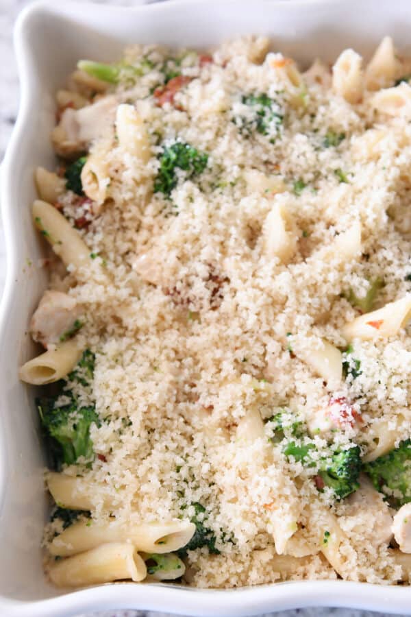 unbaked baked penne pasta in white dish with bread crumbs