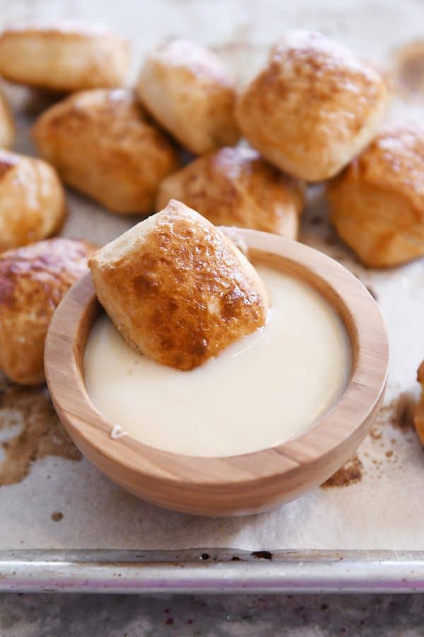 Soft pretzel bite sitting in bowl of warm cheese sauce.