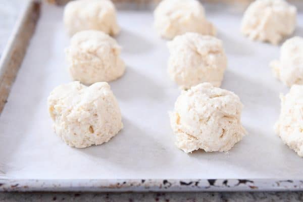 Mounds of buttermilk drop biscuits on parchment lined baking sheet.