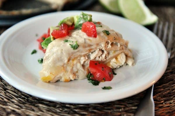 Slice of green chile chicken enchilada stack on white plate with tomatoes and cilantro.