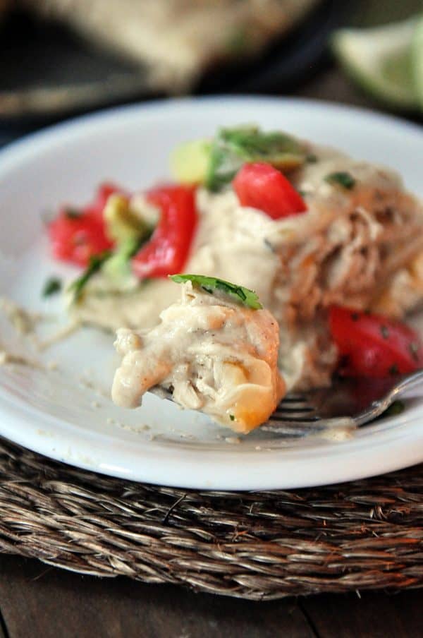 Bite of green chile chicken enchilada stack on fork on white plate.