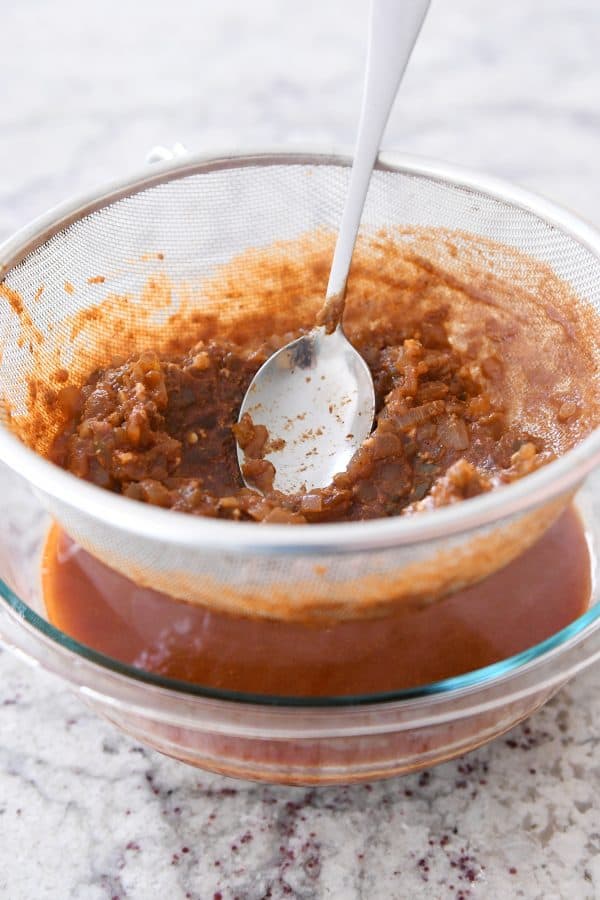 Making red sauce chicken enchiladas by pressing sauce out of veggie solids.