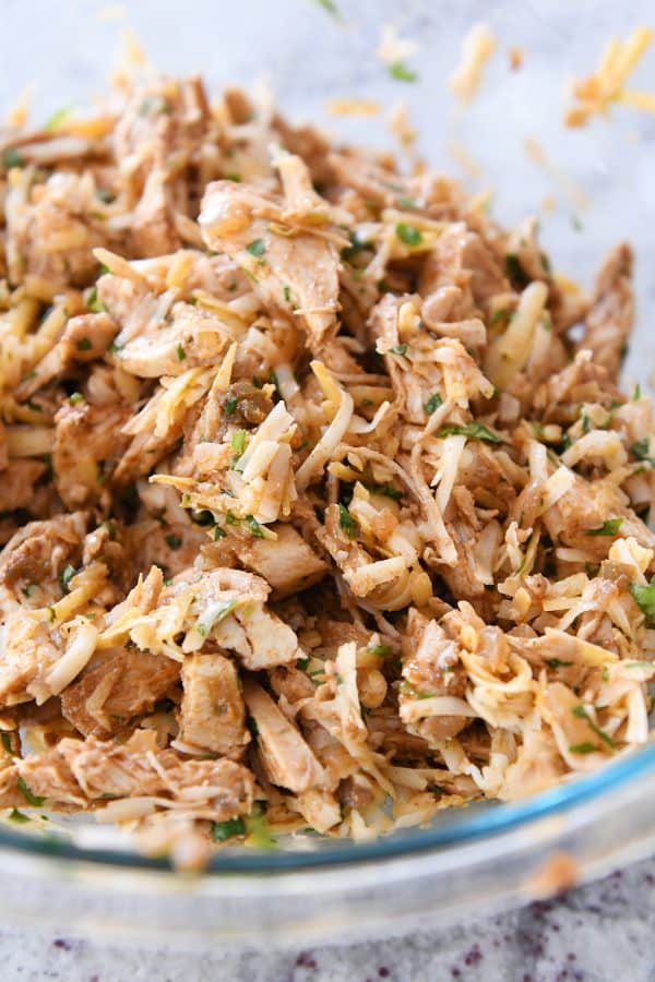 Bowl of shredded chicken and cheese for the best red sauce chicken enchiladas.