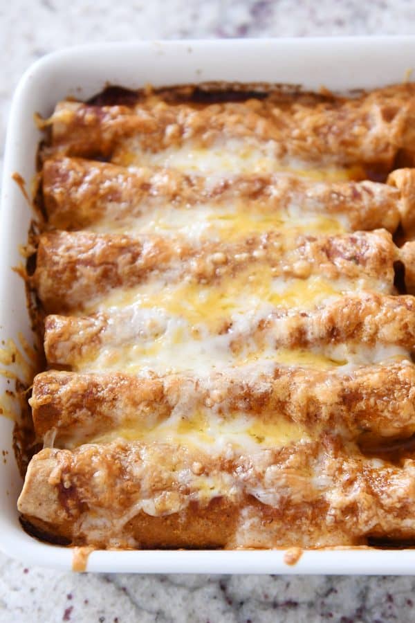 Baked pan of red sauce chicken enchiladas with lots of crusty cheese on top.