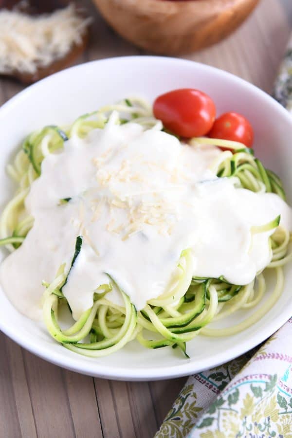 Creamy homemade alfredo sauce recipe over zoodles in white bowl.