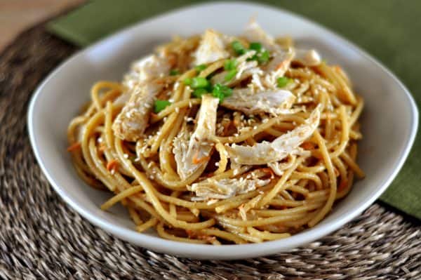 Sesame noodles topped with shredded chicken and green onions in a white bowl.