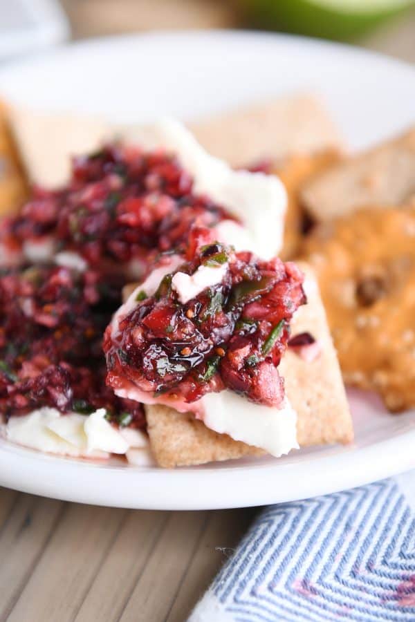 Cranberry-jalapeno cream cheese dip on wheat thin cracker on white plate.