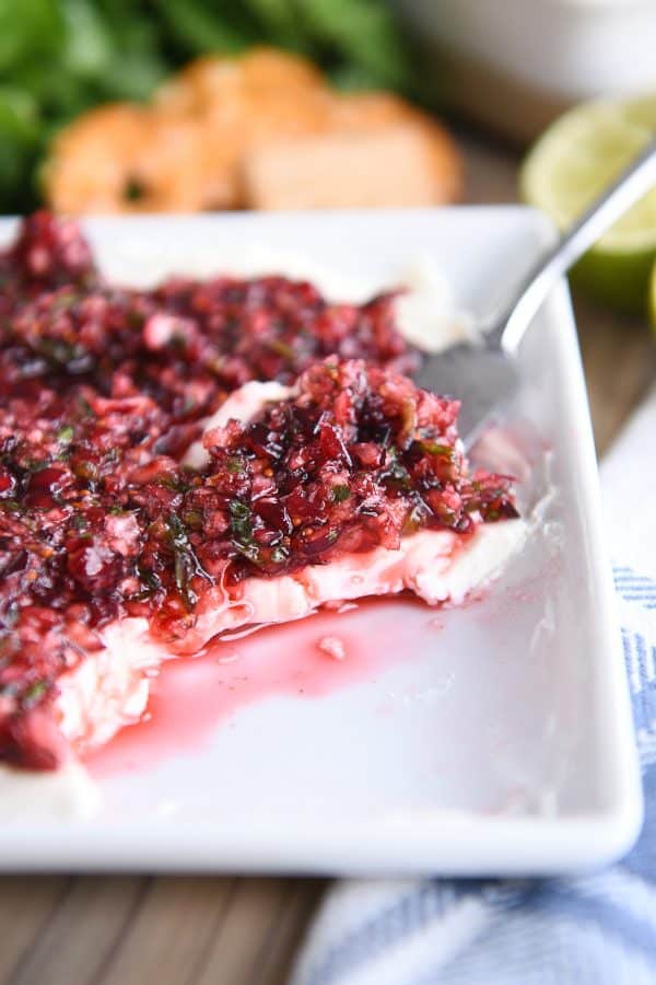 White dish with softened cream cheese topped with chopped cranberry jalapeno mixture.