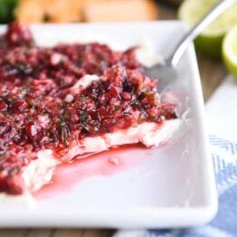 white dish with softened cream cheese topped with chopped cranberry jalapeno mixture