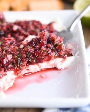 white dish with softened cream cheese topped with chopped cranberry jalapeno mixture