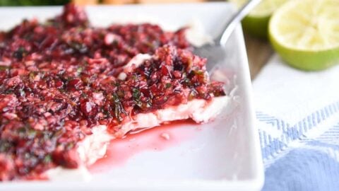 white dish with softened cream cheese topped with chopped cranberry jalapeno mixture