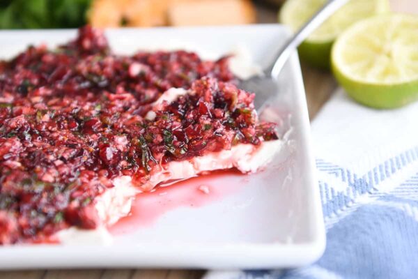white dish with softened cream cheese topped with chopped cranberry jalapeno mixture