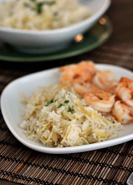White plate with cooked rice pilaf next to cooked shrimp.