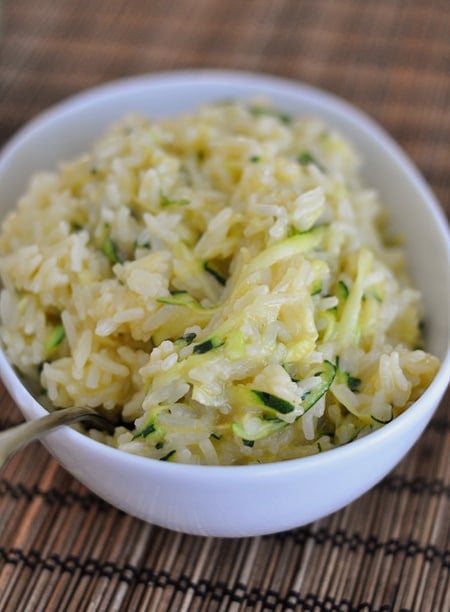 a white oval dish full of cheesy zucchini white rice with shredded zucchini in it