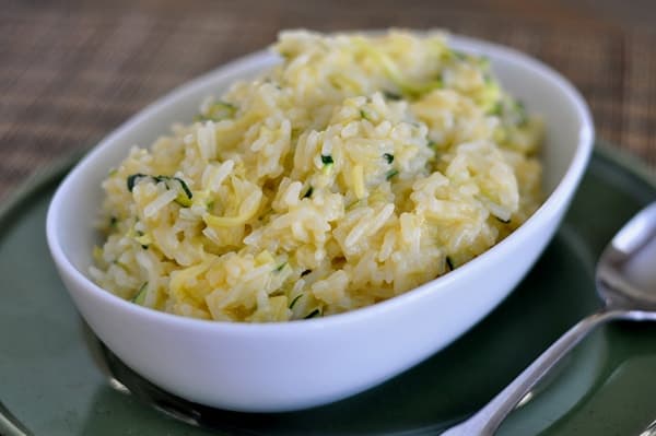 White oval bowl full of cheesy white rice with shredded zucchini in it.