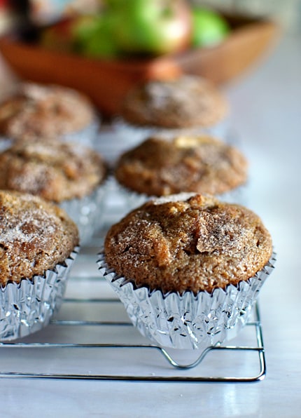 Cinnamon coated apple muffins in tin muffin liners on a cooling rack.