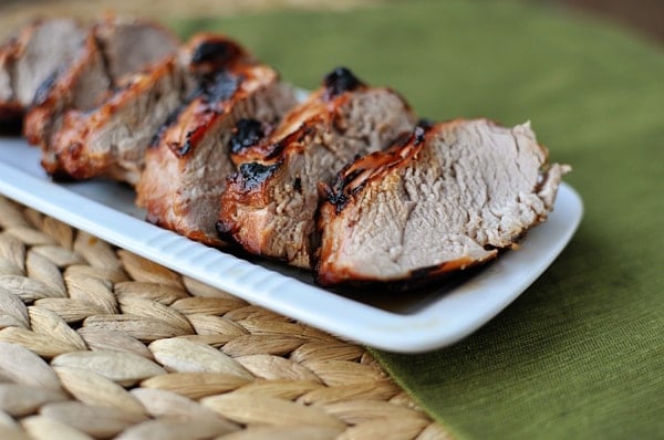 Grilled pork tenderloin cut into thick pieces and lined up on a white rectangular platter.