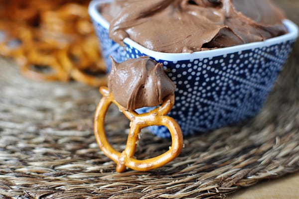 A blue ceramic bowl with chocolate dip and a pretzel in front with some dip on it.