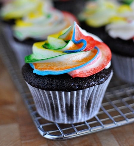 Chocolate cupcakes with tie-dye frosting on a cooling rack.