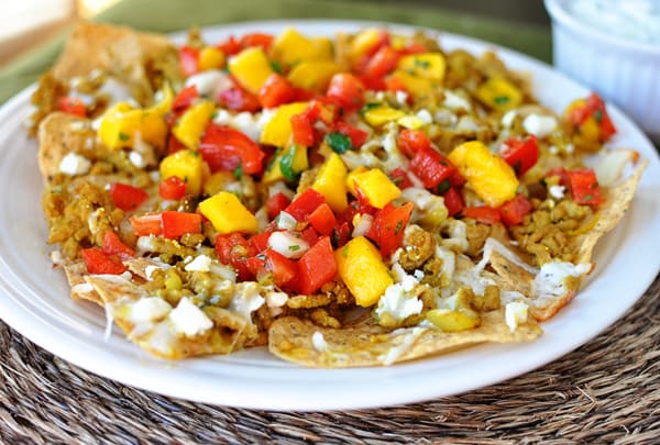 White plate full of nachos with mango salsa on top.