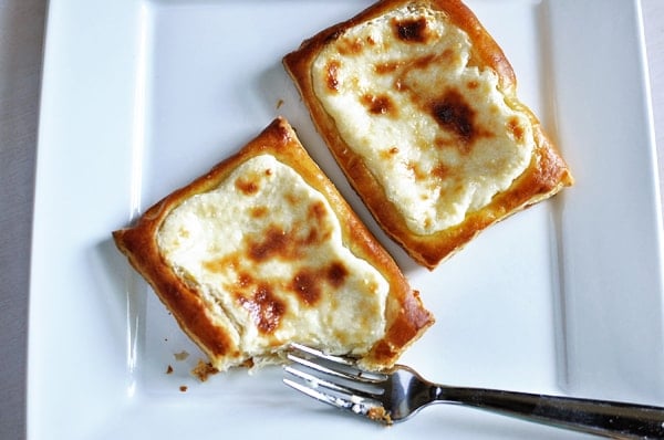 Top view of two cheese danishes on a white plate, one with the corner cut off.