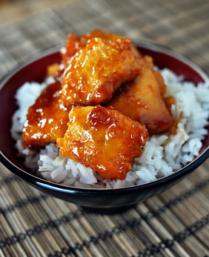 Bowl with white rice topped with big pieces of sticky red sauce chicken.