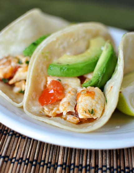 Corn tortilla fish tacos with diced tomatoes and sliced avocados on top.