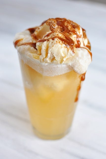 Clear glass with a caramel apple cider ice cream float drizzled with caramel sauce.