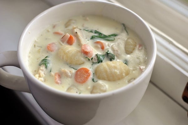 Chicken gnocchi and vegetable soup in a white mug.