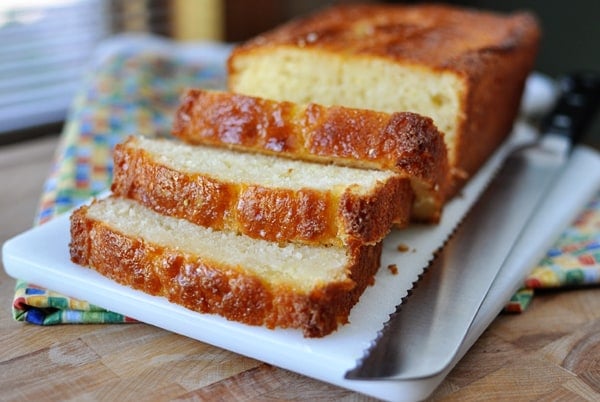 A loaf of lemon bread with three thick slices cut off on a white platter.