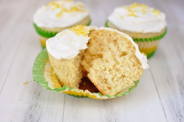 A lemon cupcake with white frosting and lemon zest split in half on a muffin liner.