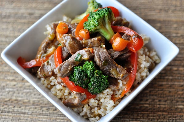 Top view of a square white bowl with cooked rice, veggies and strips of beef.