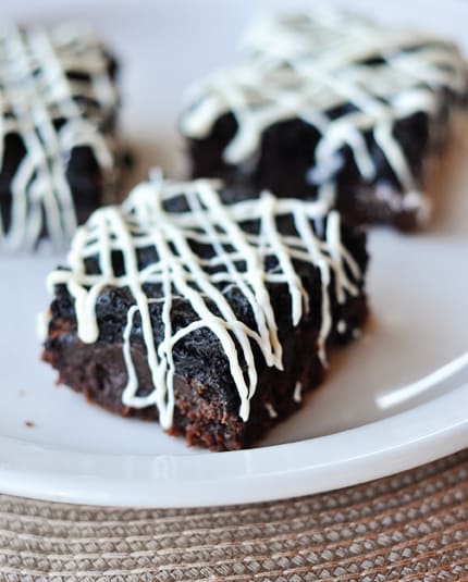 Three oreo truffle brownies with white chocolate drizzle on white plate.